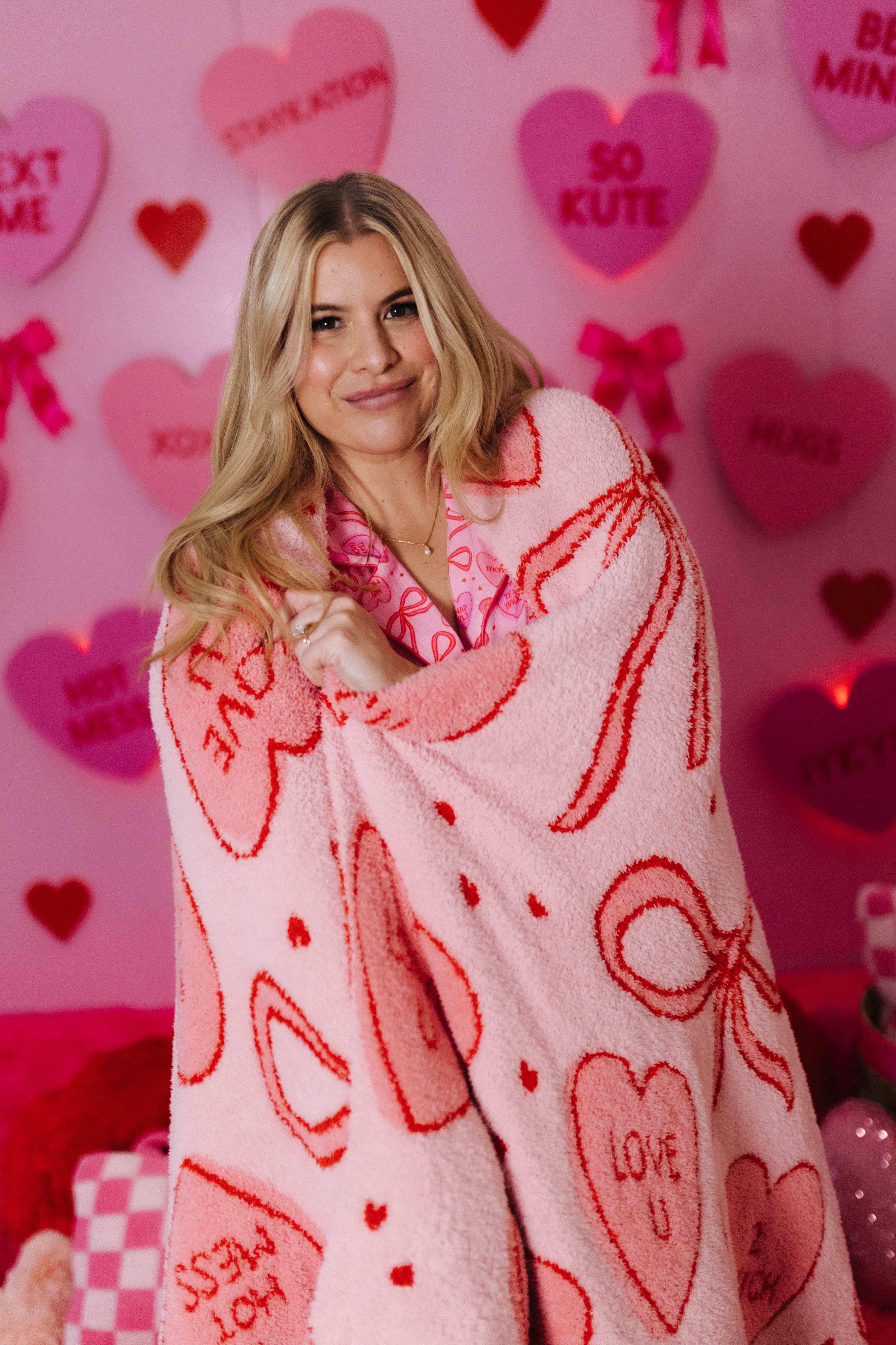 Woman wrapped in a heart-patterned blanket against a pink background with hearts and text.