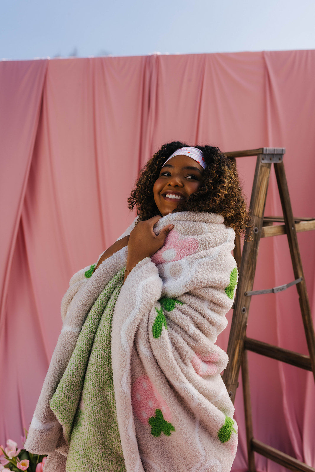 Woman wrapped in a blanket with pink and green patterns against a pink backdrop