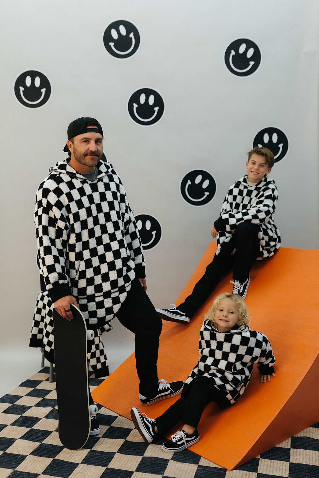 Two adults and a child in matching checkered outfits on an orange platform with smiley face patterns.