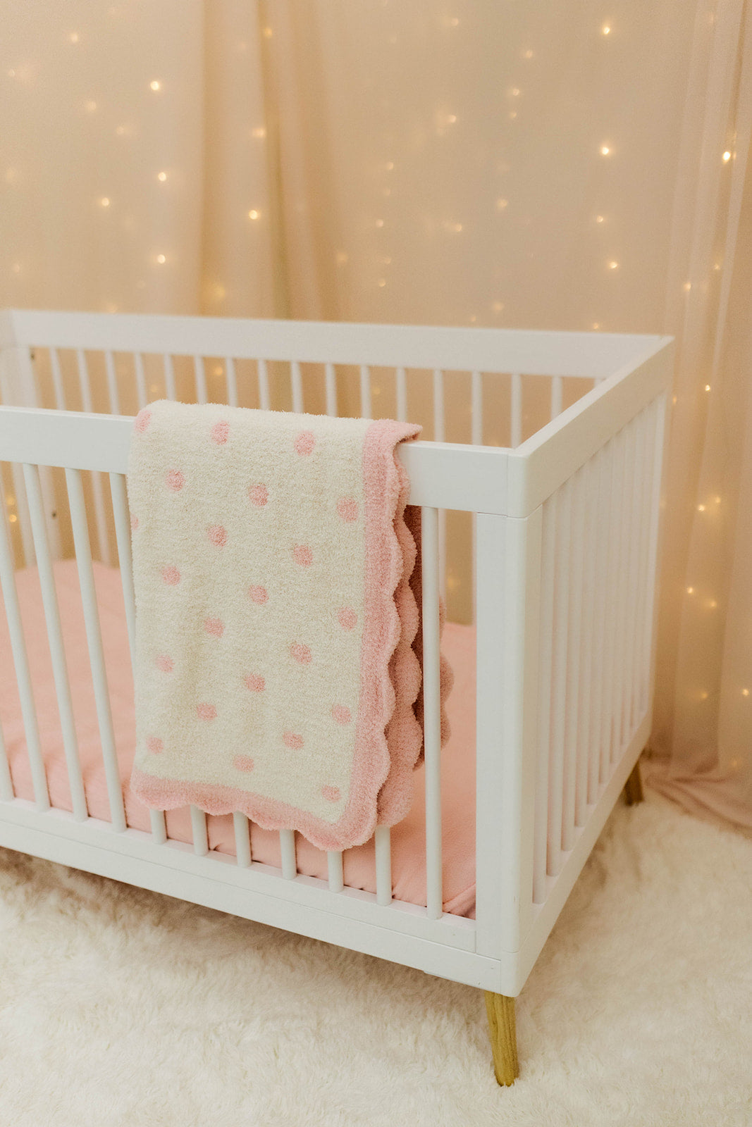 White crib with pink blanket against a softly lit curtain background