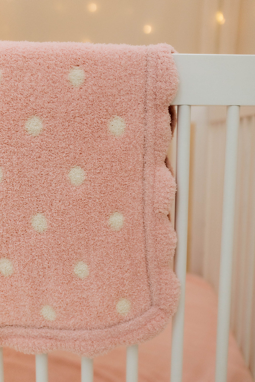 Pink polka dot blanket draped over a crib with a soft focus background