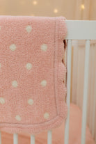 Pink polka dot blanket draped over a crib with a soft focus background