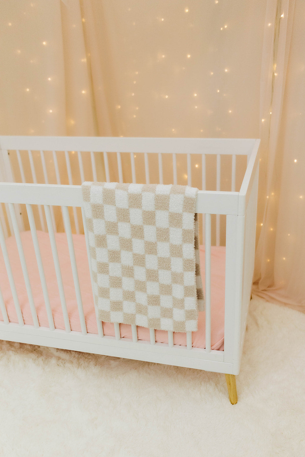 White crib with sand and white checkered blanket against a softly lit curtain background
