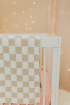 Checkered blanket draped over a crib with a soft, blurred background