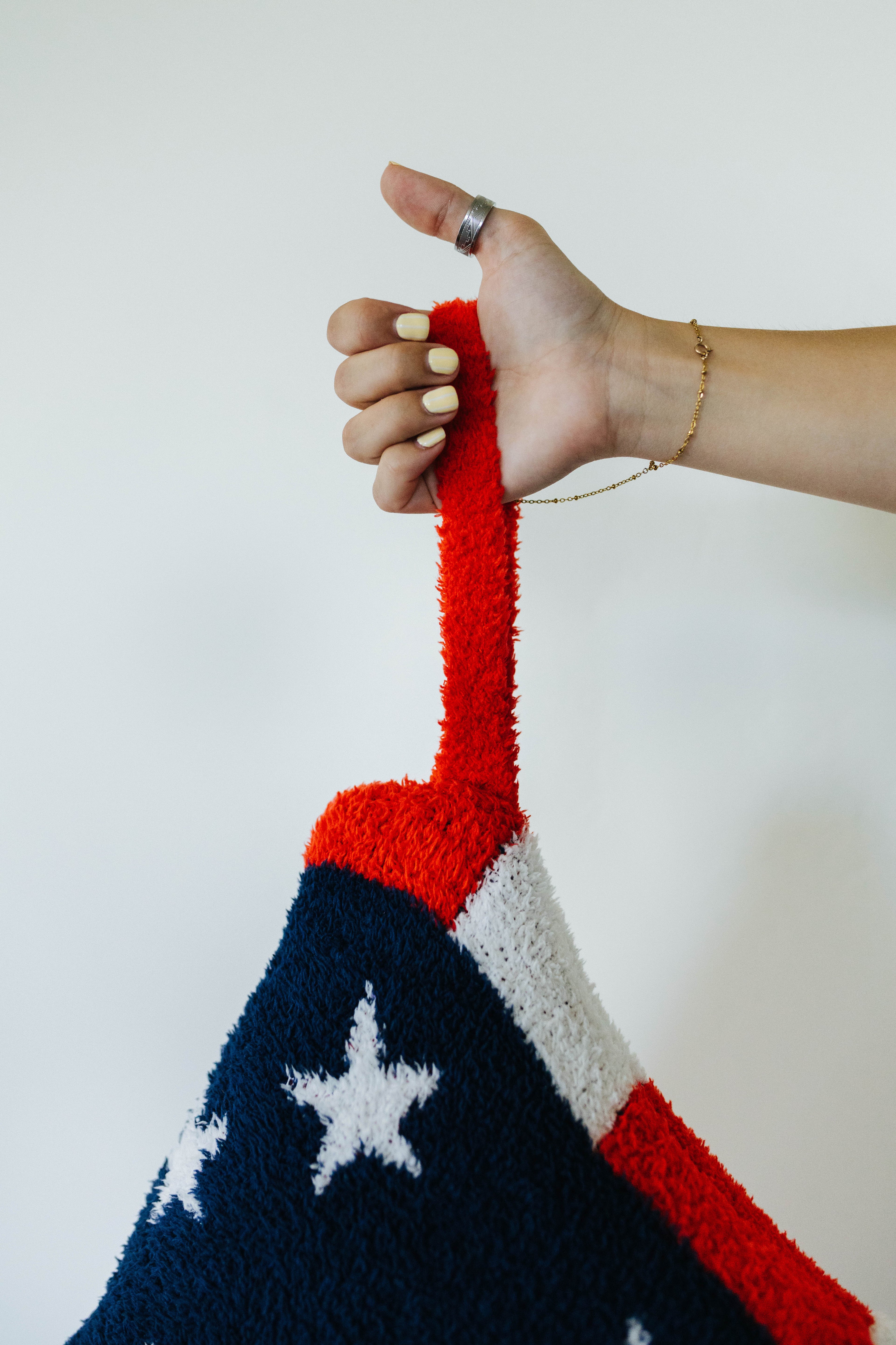 Hand holding a red, white, and blue quillow item against a plain background