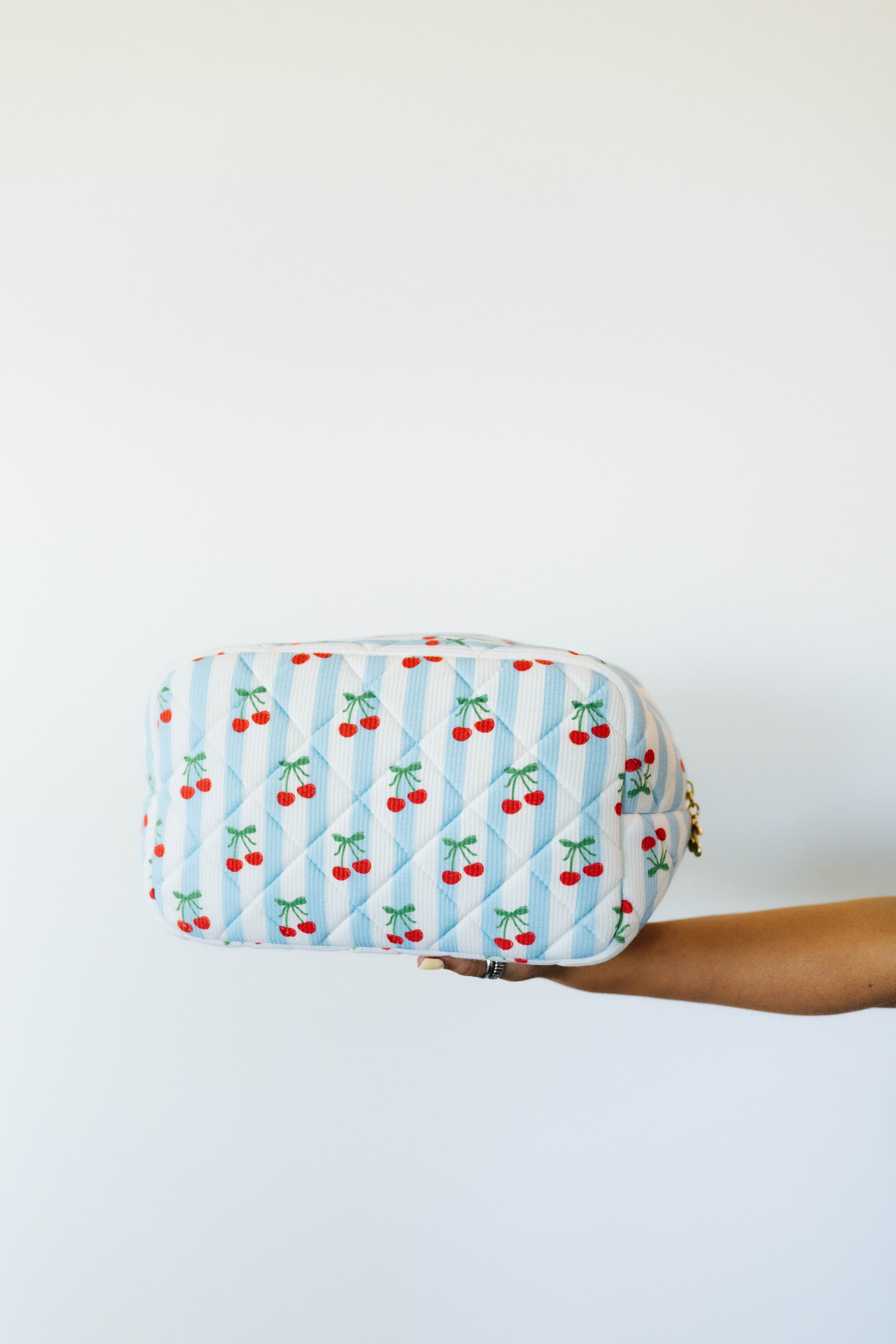 Fabric pouch with cherry pattern held by a person against a white background