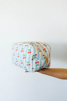 Hand holding a quilted fabric pouch with striped pattern and cherry design on a white background