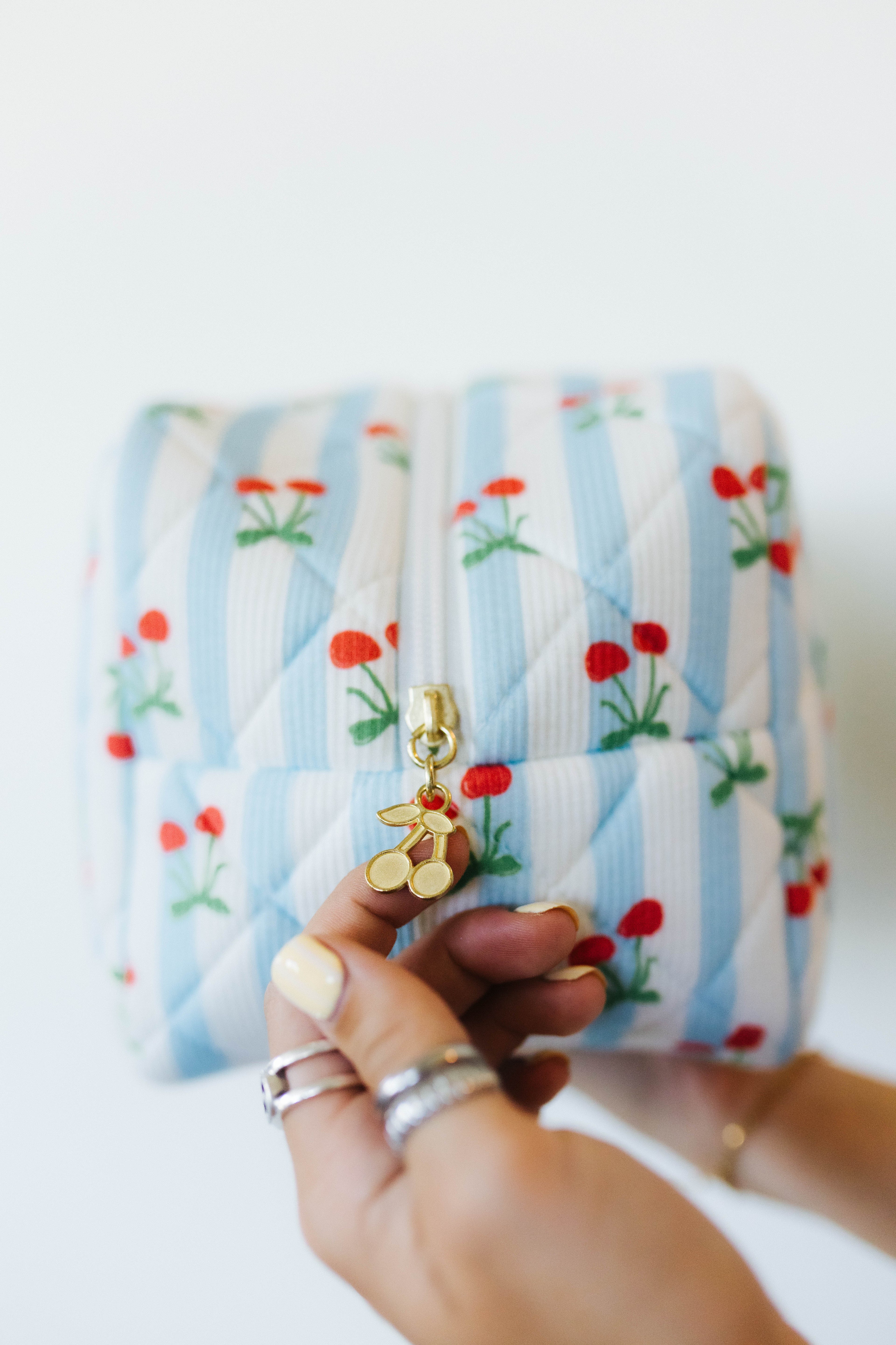 Quilted pouch with cherry design held by a hand against a white background