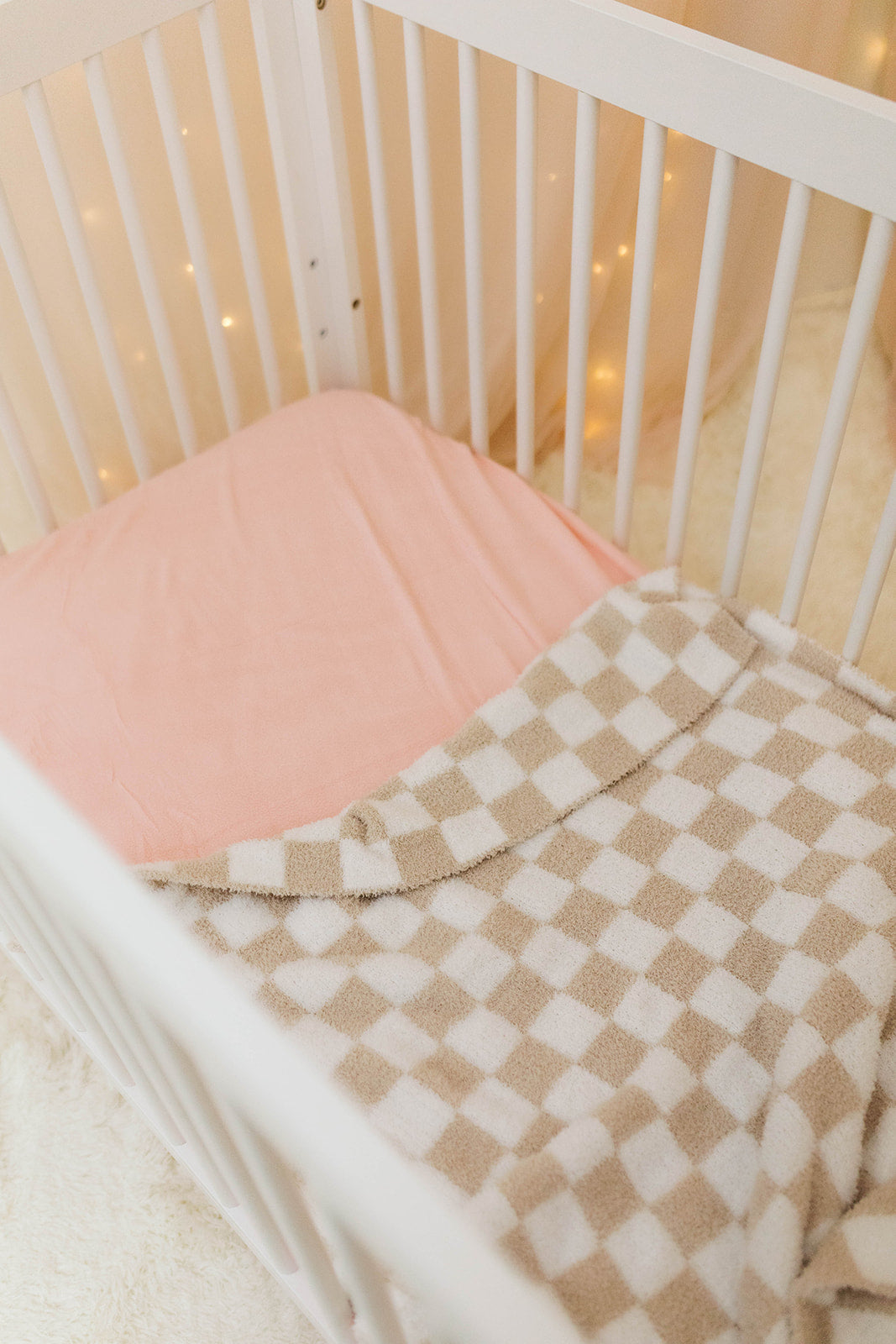Crib with pink mattress and checkered blanket in a softly lit room