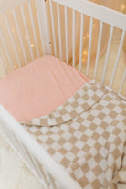 Crib with pink mattress and checkered blanket in a softly lit room