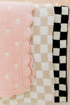 Three textured baby blankets in pink with white polka dots, beige checkered, and black and white checkered patterns.