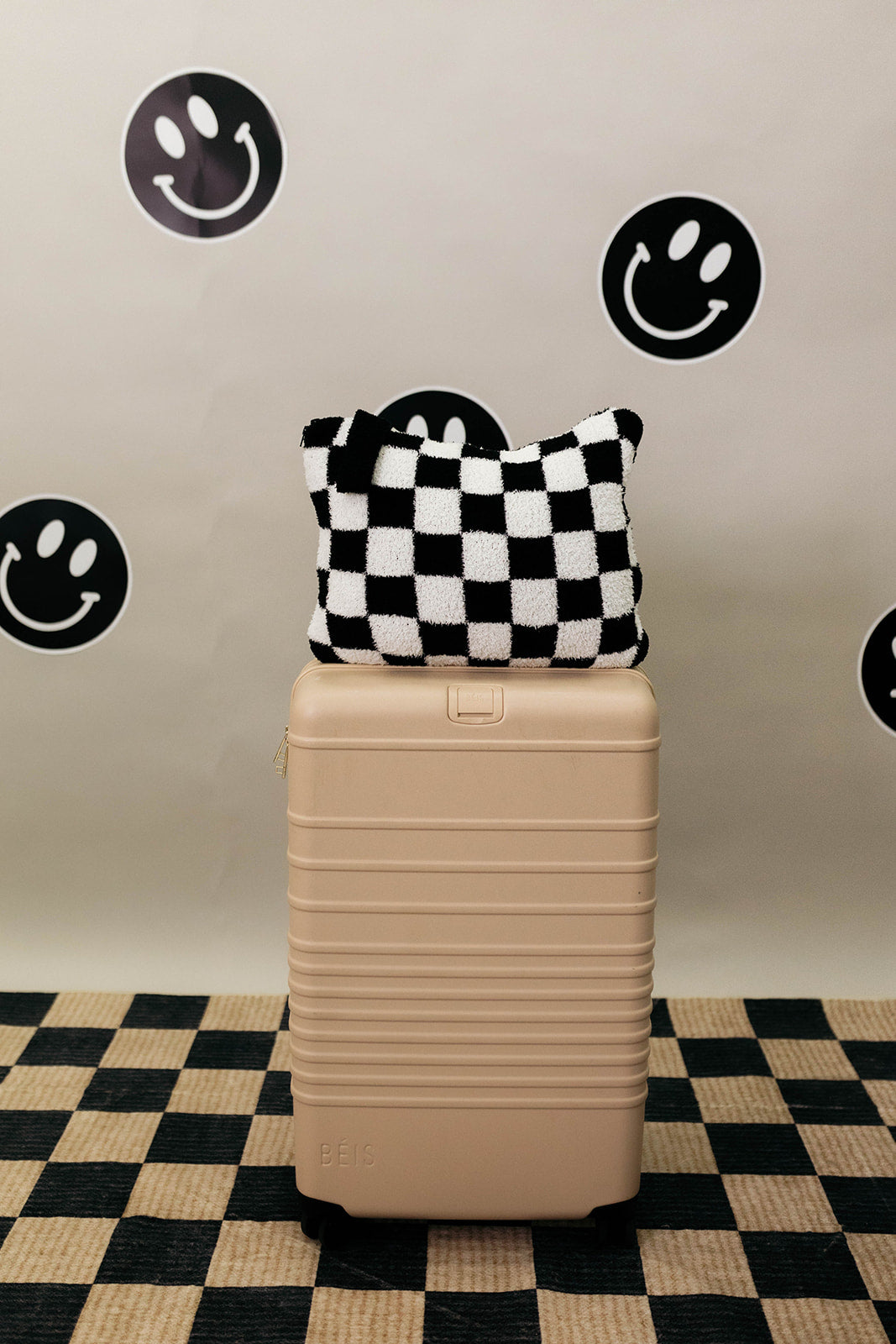 Beige suitcase with a checkered quillow on top against a wall with smiley face stickers.