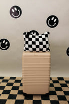 Beige suitcase with a checkered quillow on top against a wall with smiley face stickers.