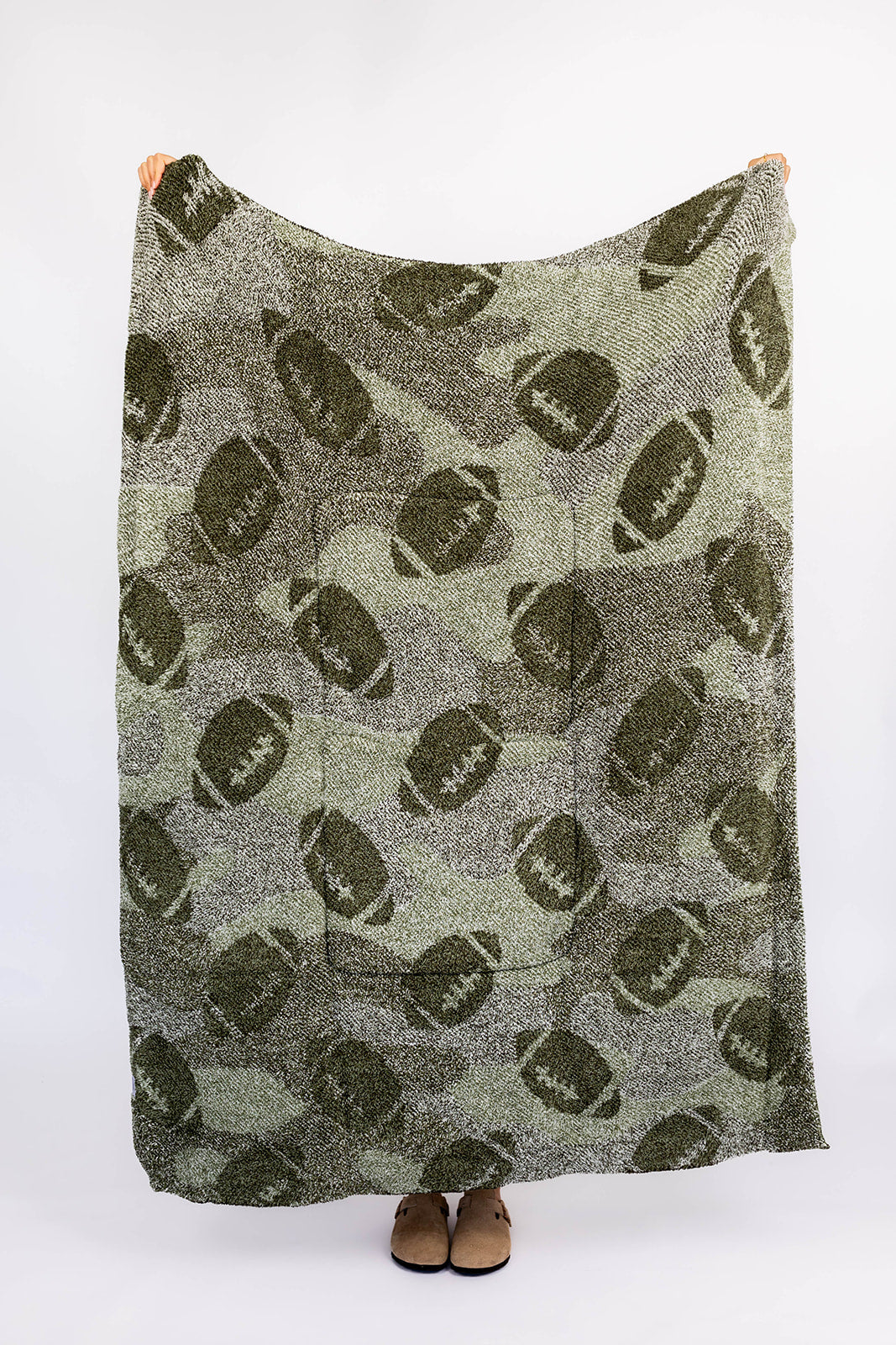 Green blanket with football pattern draped over a person on a white background