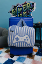 Blue suitcase with a striped quillow featuring a game controller design on a colorful rug.