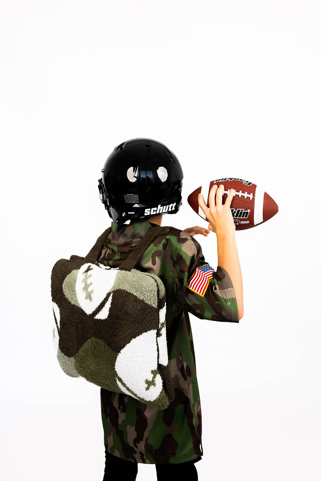Person wearing a camouflage outfit and helmet, holding a football on a white background with football quillow