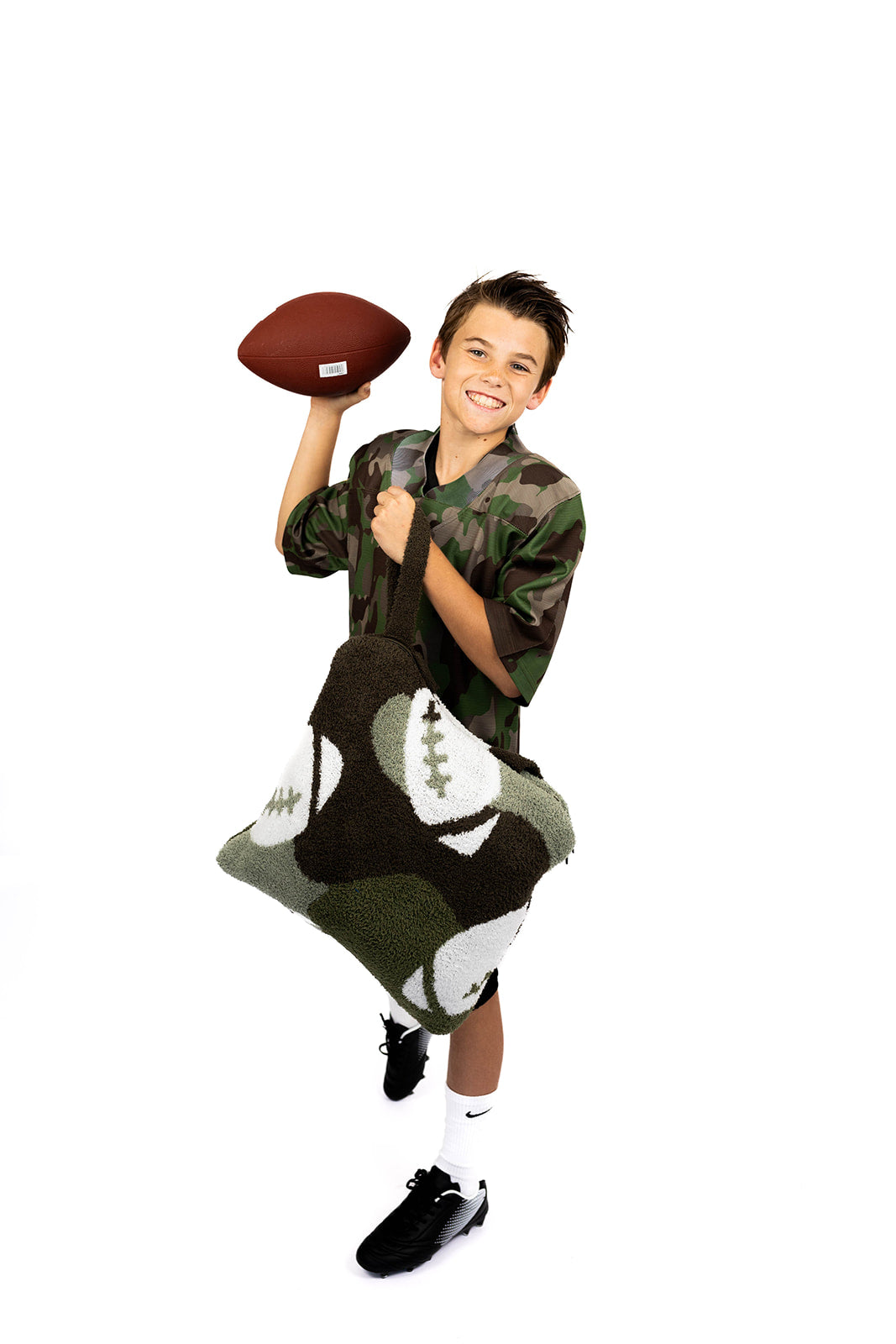 Child in camouflage sports outfit holding a football with a football backpack quillow on a white background
