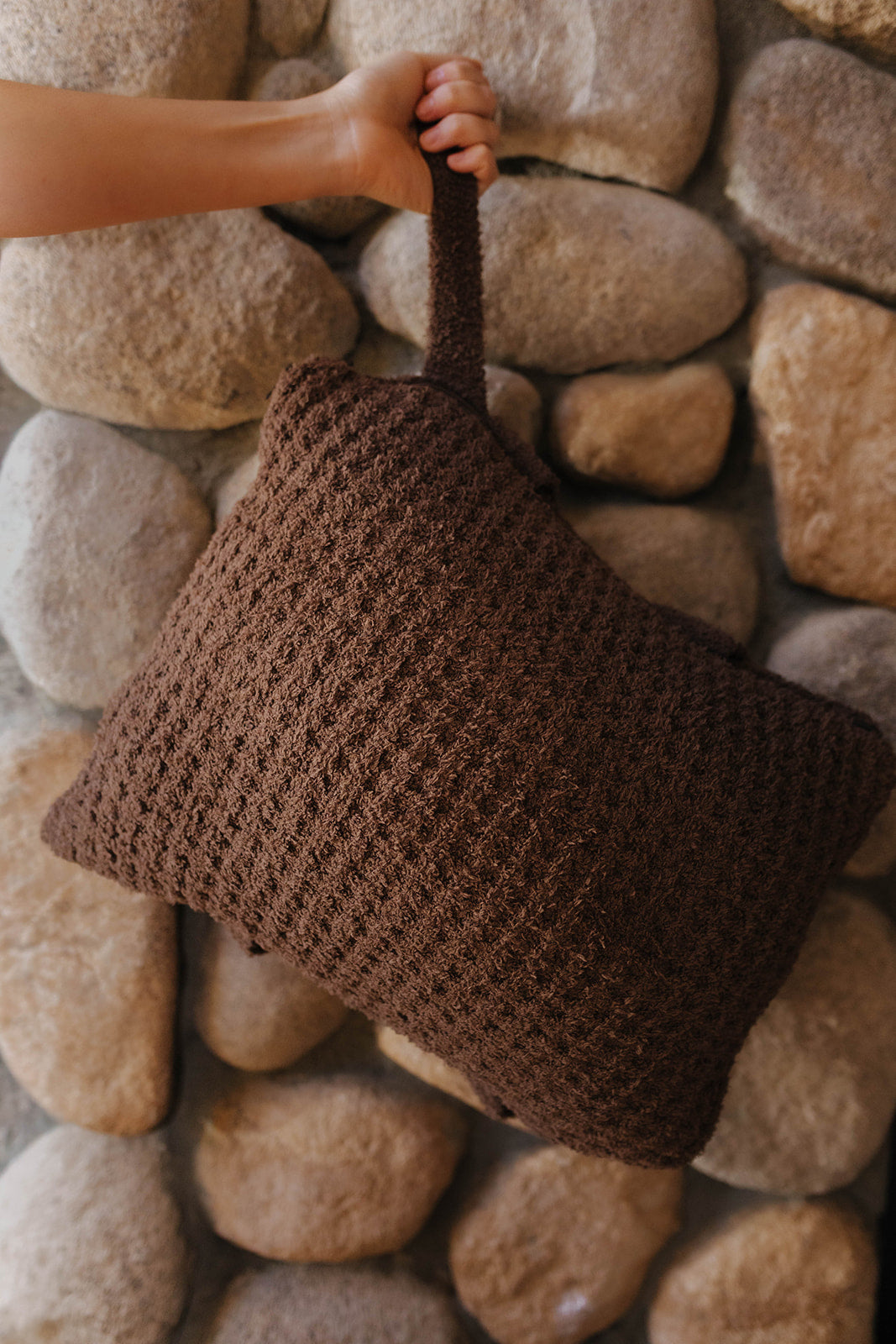 Brown waffle quillow folded into a pillow and held by its wrist strap.