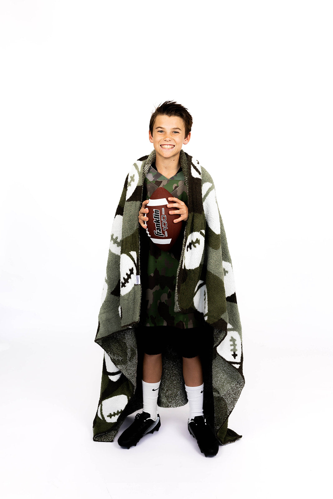 Person wrapped in a patterned camo football blanket holding a football on a white background
