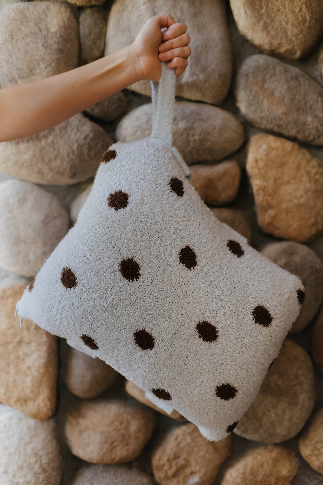 Blue and brown polka dot quillow folded and held by its wrist strap.