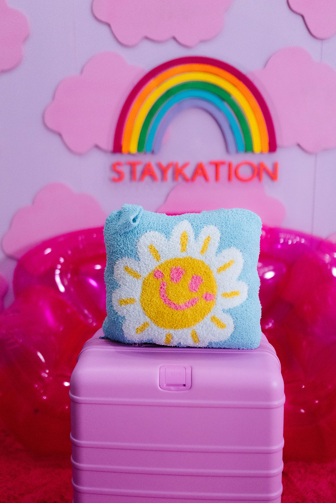 Blue quillow with a sun design on a pink suitcase against a colorful background