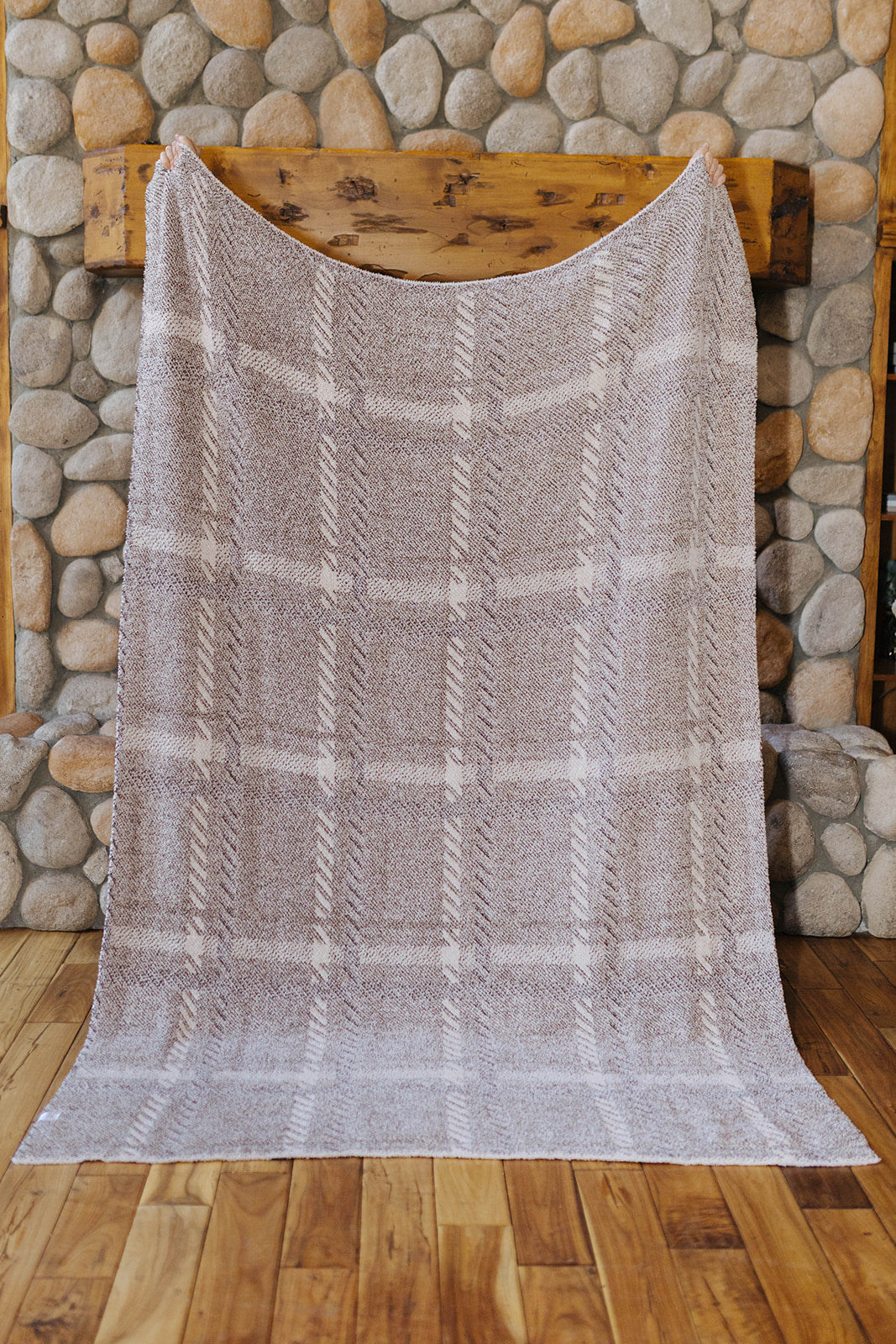 Reverse of the plaid blanket held open by a stone fireplace.