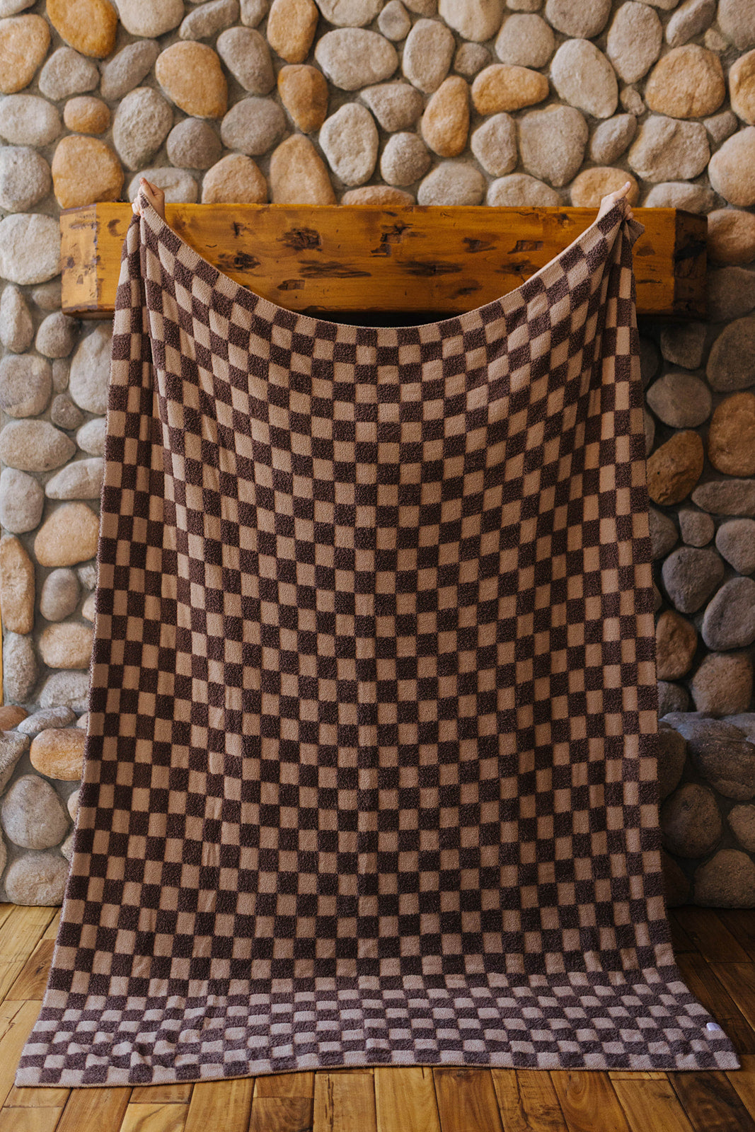 Brown check blanket held open at full size in front of a stone fireplace.
