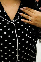 Person wearing a black outfit with white heart patterns, holding a hand with a ring.