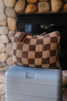 Folded brown check quillow resting on a suitcase.