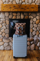 Brown check quillow displayed with its backpack straps on a suitcase.