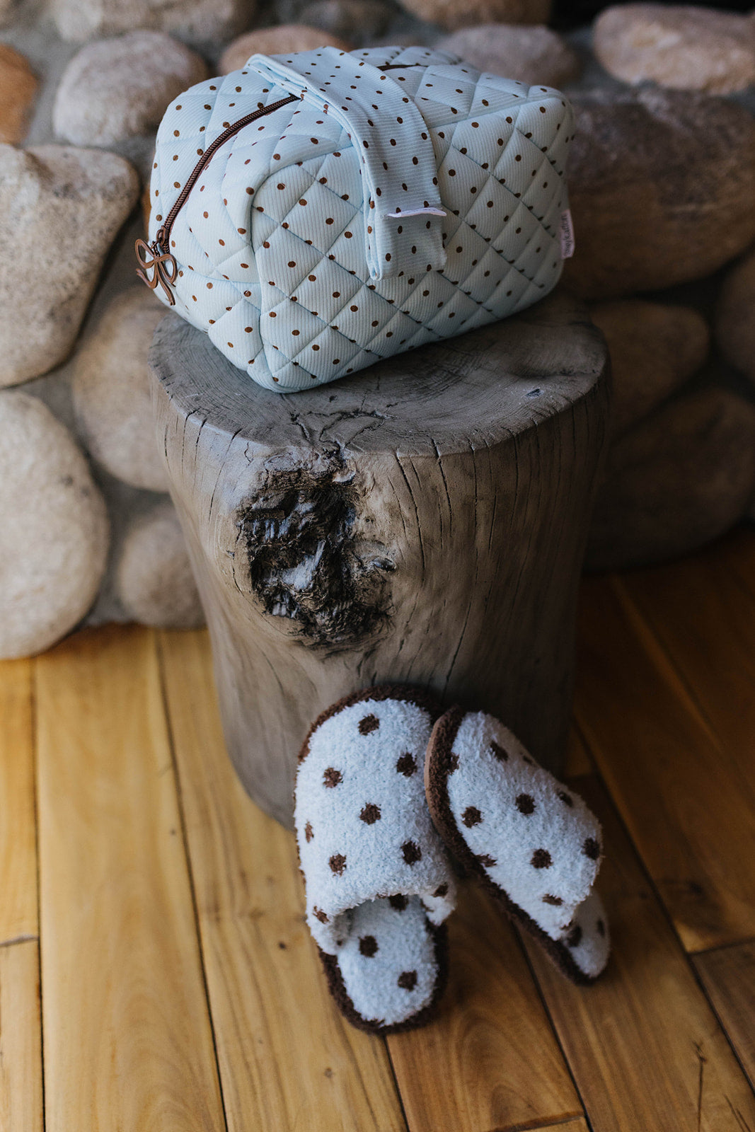 Blue polka dot cosmetic bag and matching slippers on a wood stool.