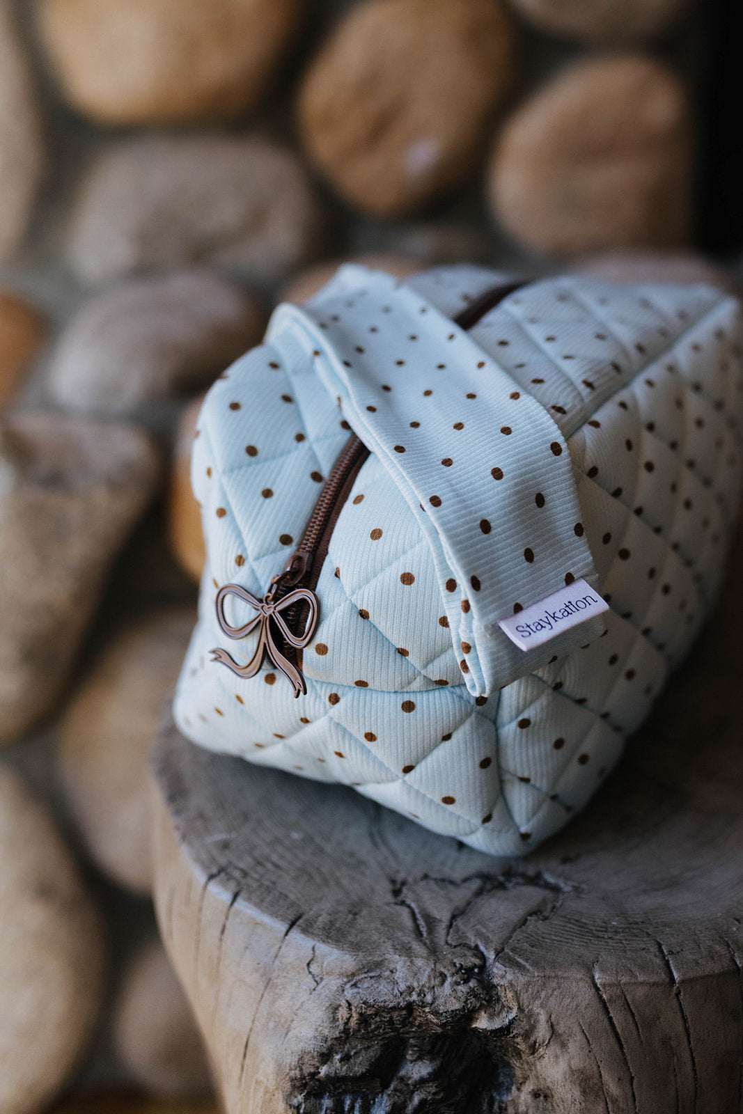 Quilted blue polka dot cosmetic bag displayed on a wood stool.