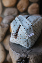Quilted blue polka dot cosmetic bag displayed on a wood stool.
