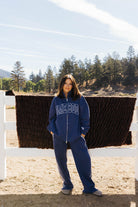 Full length front view of the blue Homebody zip sweatshirt and side stripe sweatpants beside a fence.
