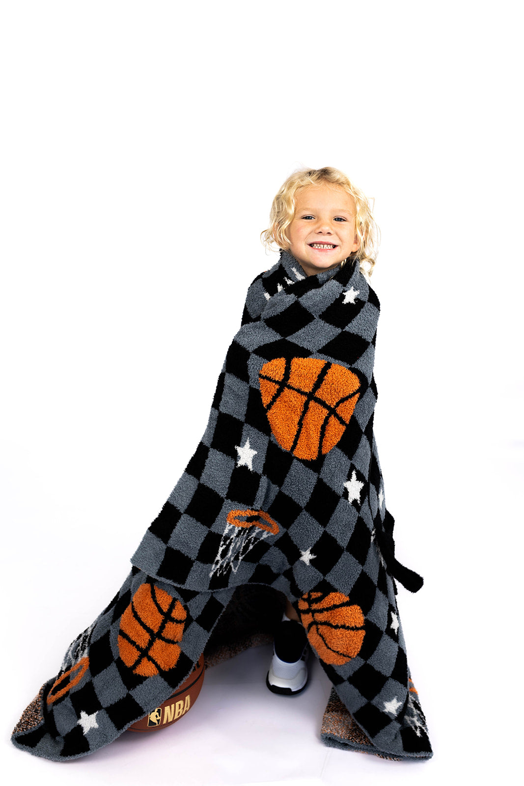 Child wrapped in a blanket with basketball patterns on a white background