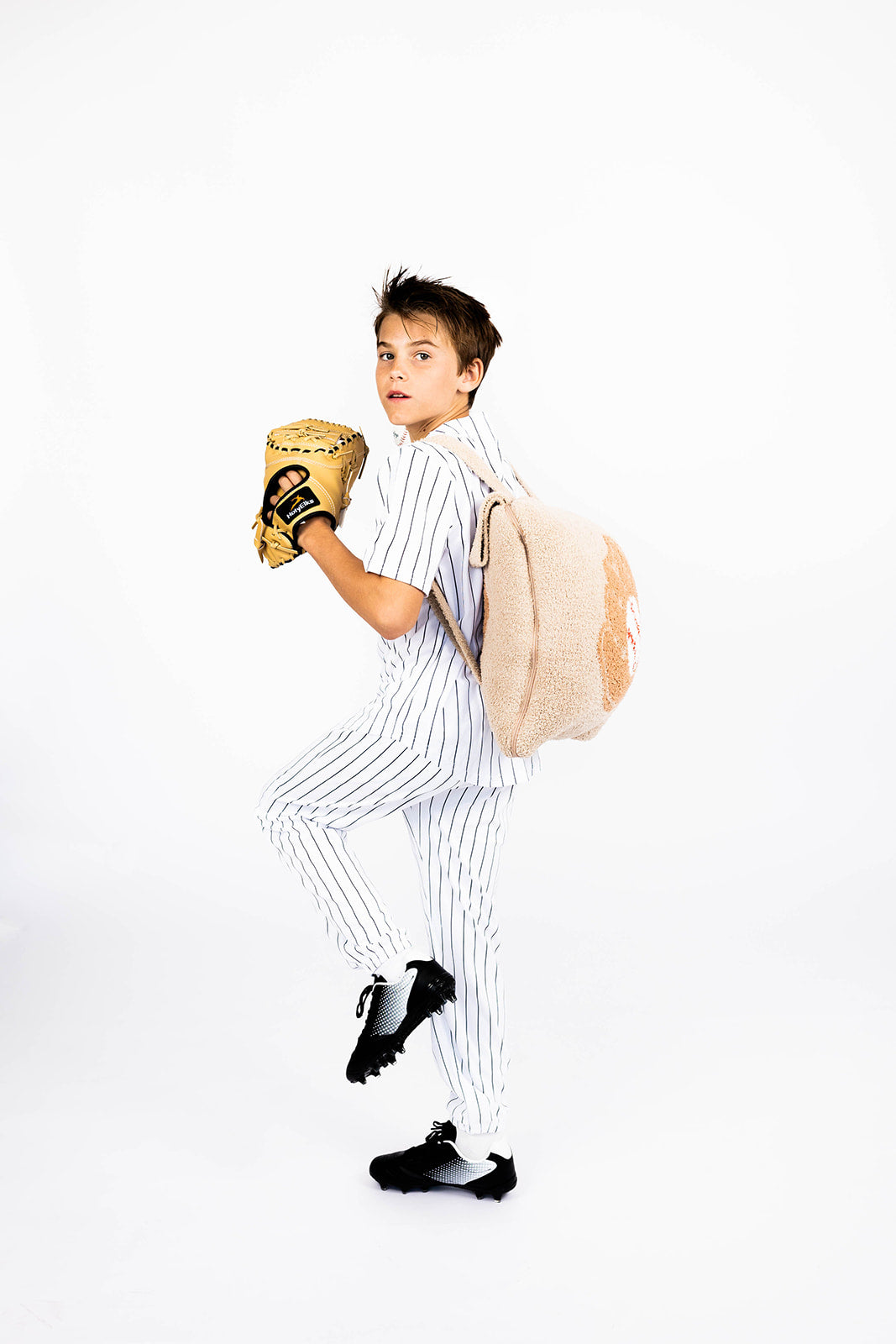 Boy in a baseball uniform holding a glove and a baseball quillow on a white background