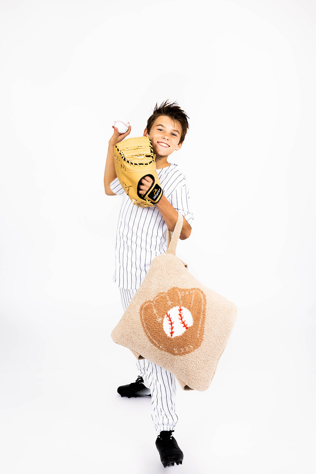 Child holding a baseball glove and a quillow with a baseball design on a white background