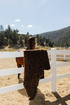 Chocolate brown faux fur blanket draped over a white fence beside a horse.