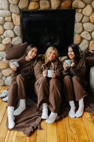 Brown waffle quillow pillows beside three seated models in matching brown apparel.
