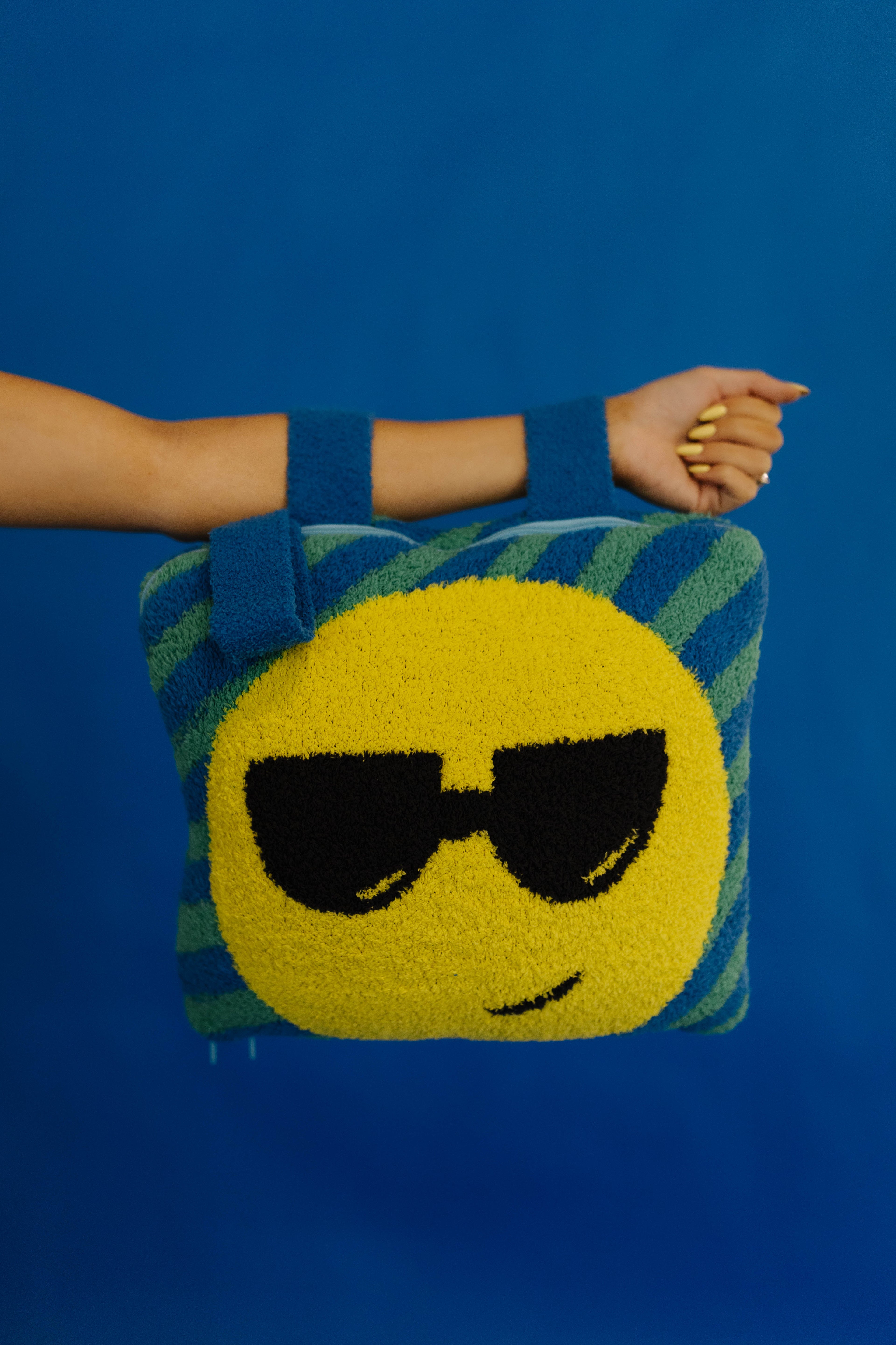 A person's arm and hand holding a quillow with black sunglasses and blue striped sides, set against a solid blue background.