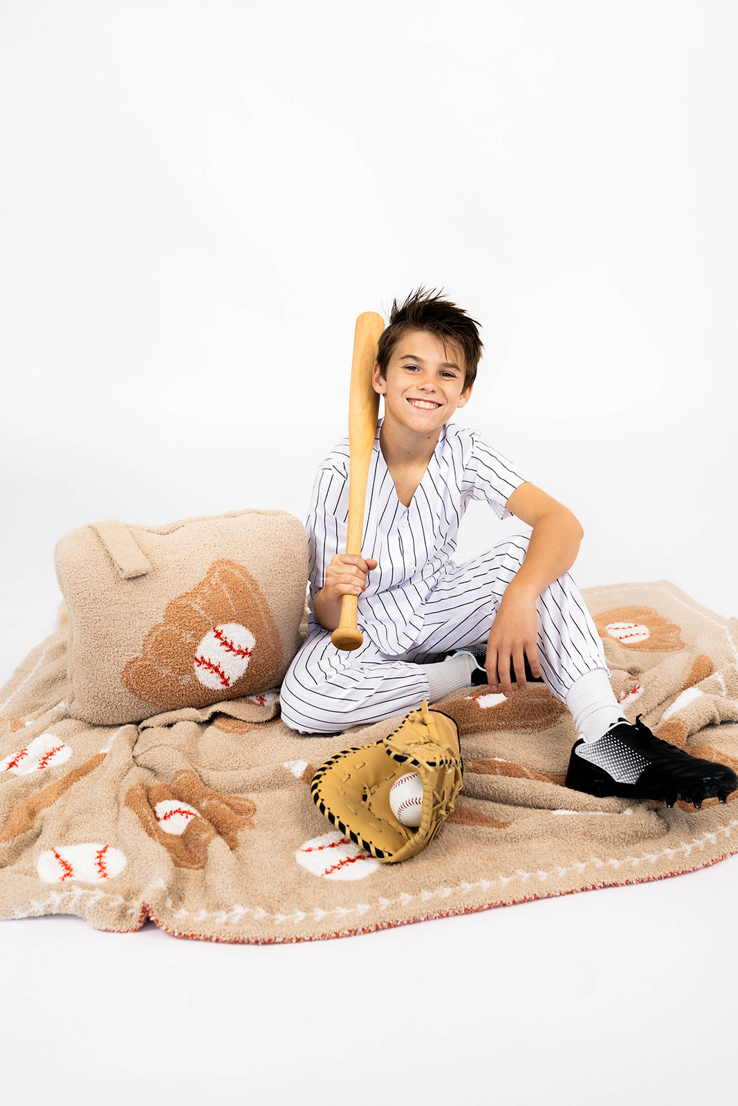 Child in a baseball-themed outfit with a bat and baseball glove on a blanket