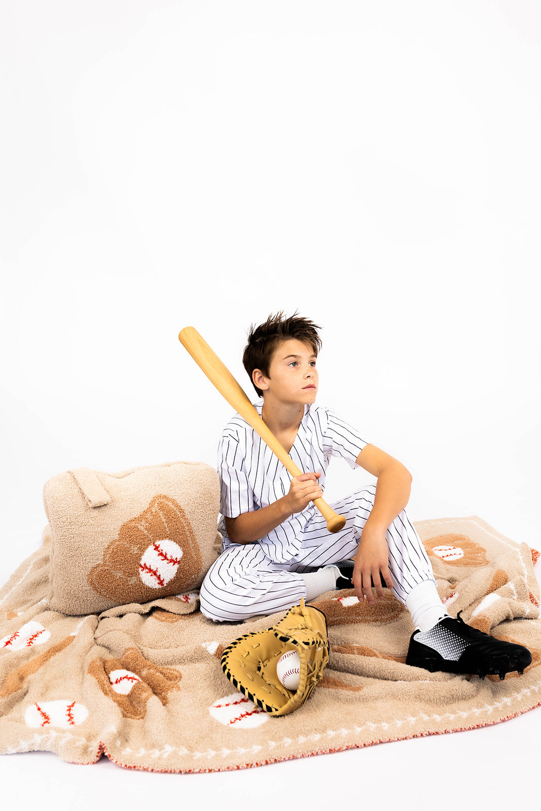 Person in a striped shirt sitting on a baseball blanket with a baseball bat and glove 