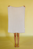 Person holding a white and beige striped kid blanket against a yellow background