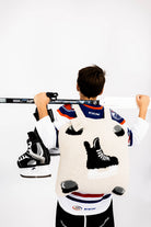 Person wearing a hockey jersey with a unique design and wearing hockey quillow, holding a hockey stick on a white background