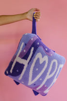 holding the quillow by the wristlet strap on a solid back background