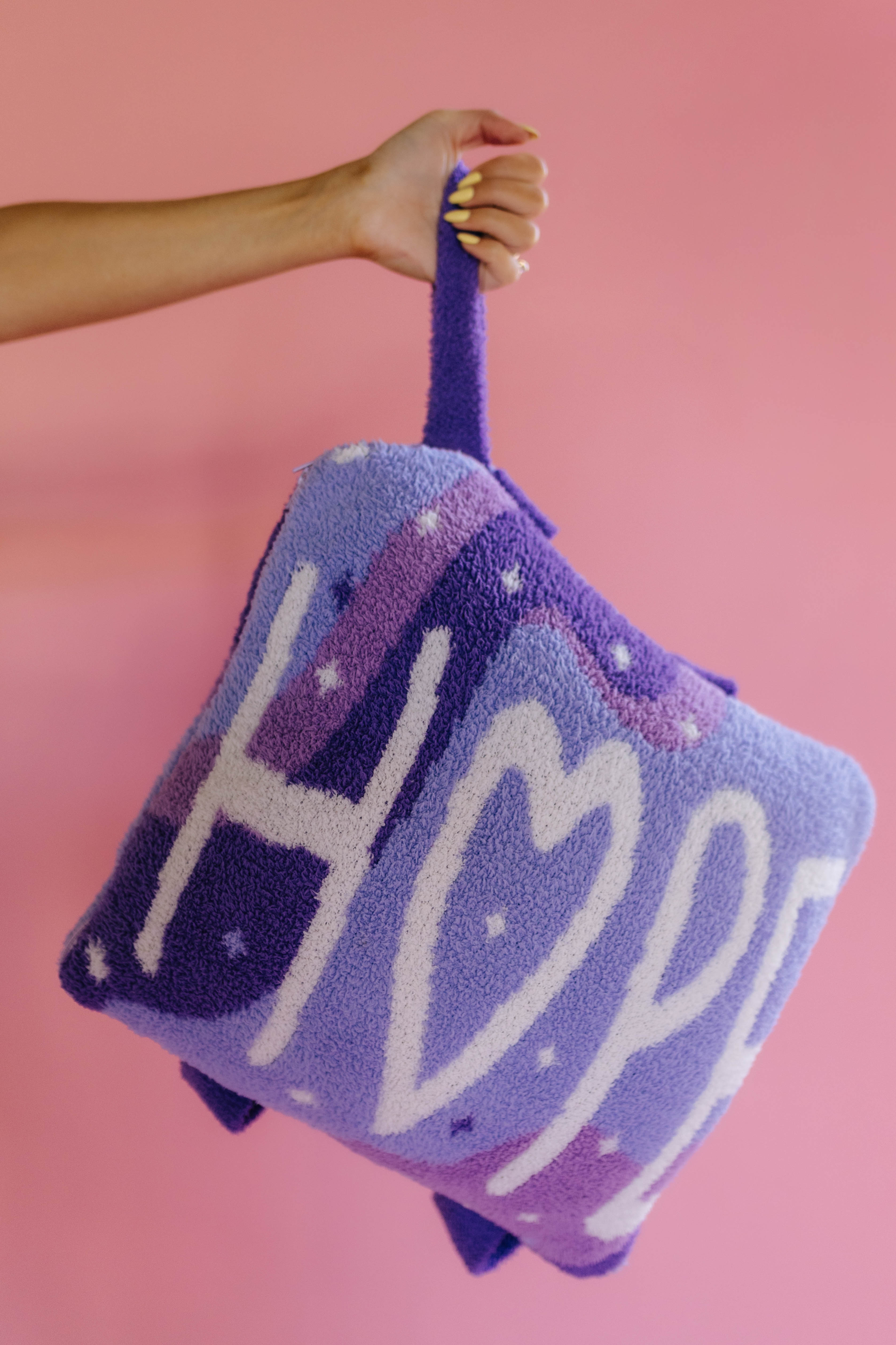 holding the quillow by the wristlet strap on a solid back background