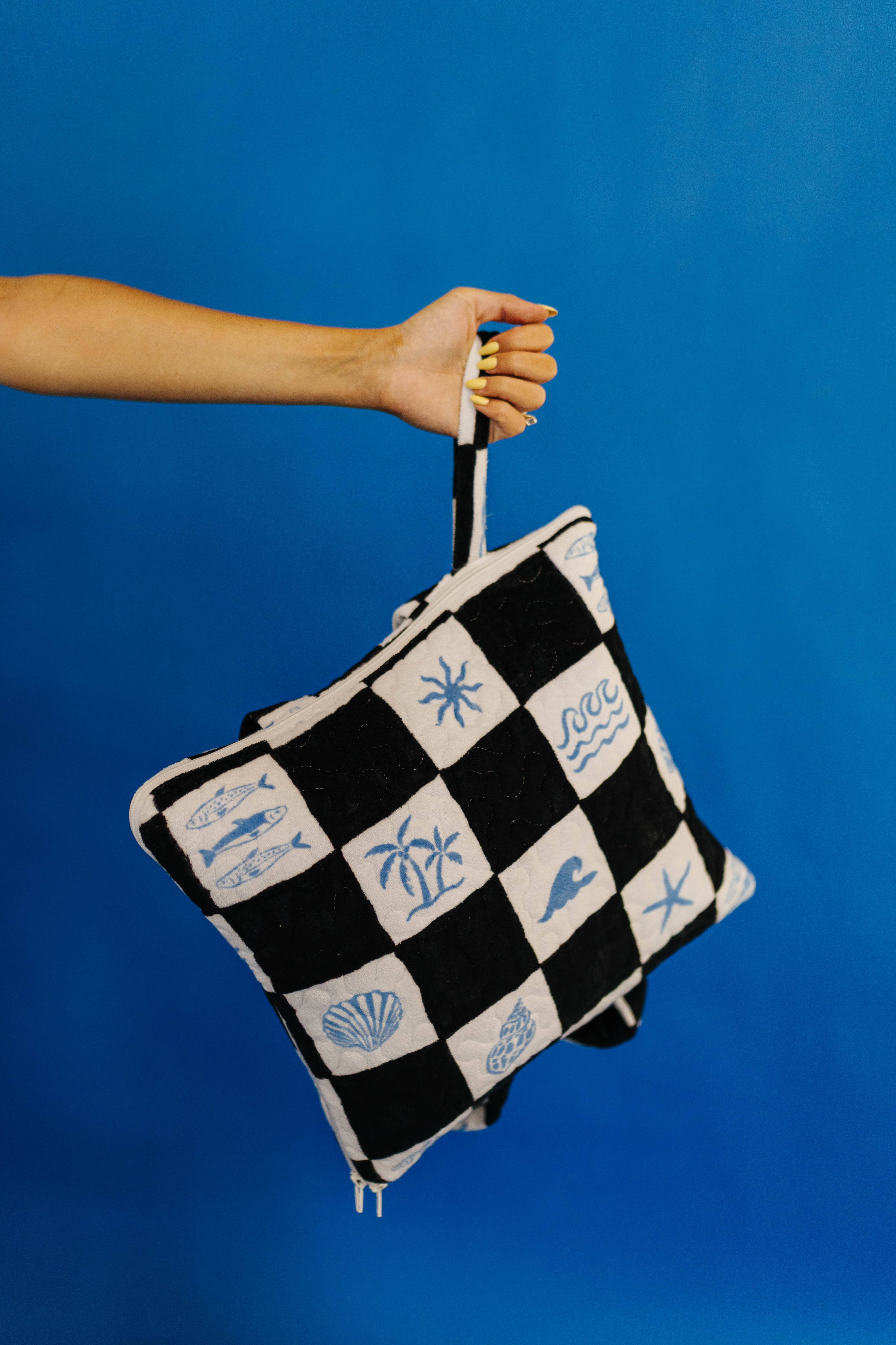 Checkered outdoor quillow with beach-themed patterns held against a blue background