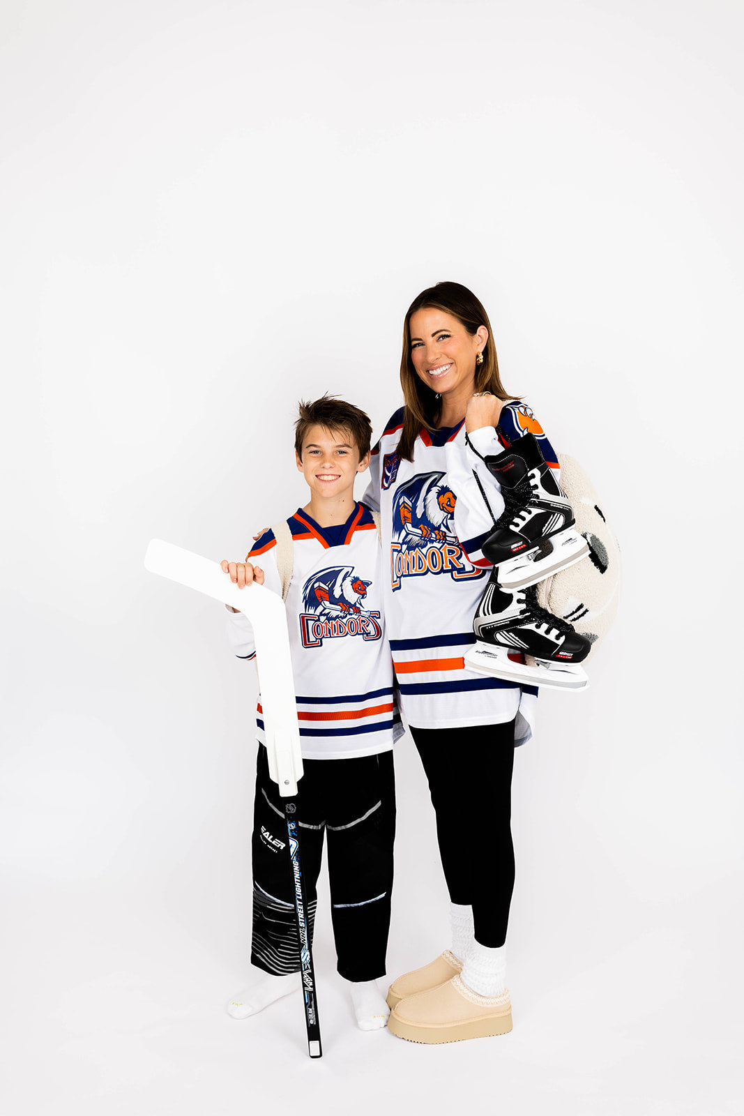 Woman and child wearing hockey-themed clothing holding skates and a hocky quillow on a white background