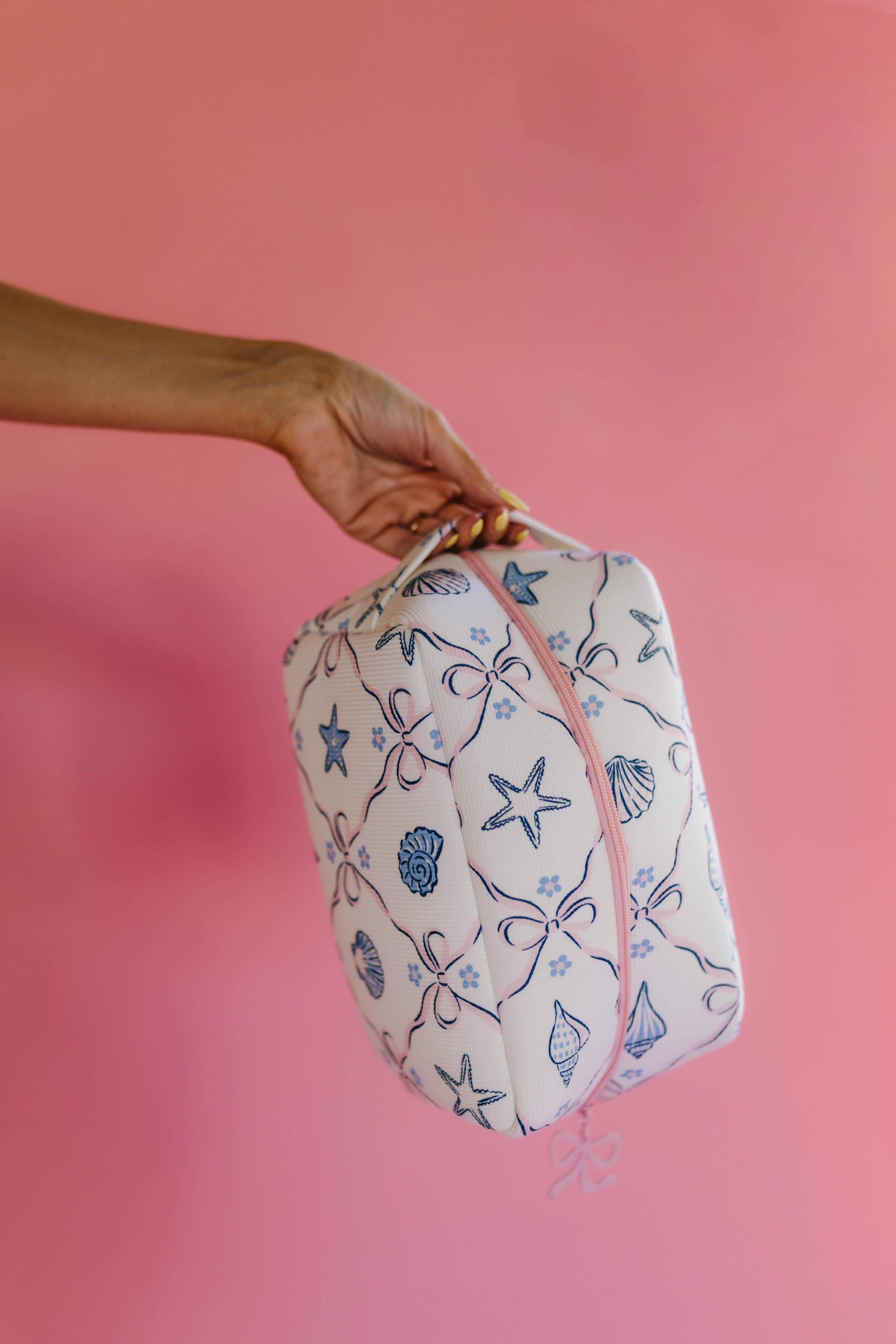 Hand holding a patterned bag against a pink background