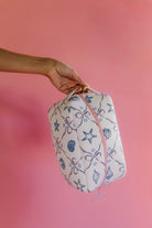 Hand holding a patterned bag against a pink background